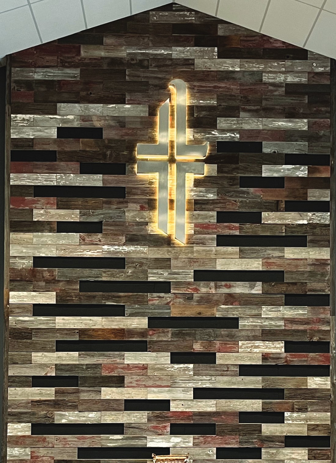 The illuminated cross on the reclaimed-wood wall at the front of our sanctuary